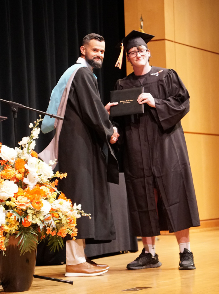 A graduate accepts his diploma from the high school principal during a summer graduation.