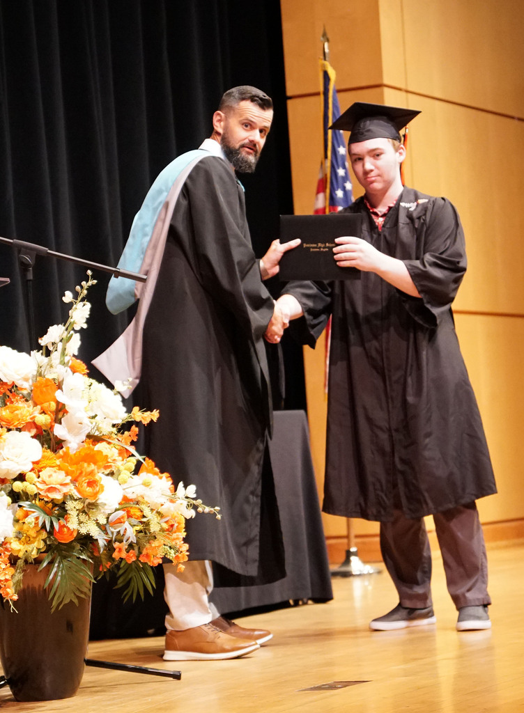 A graduate accepts his diploma from the high school principal during a summer graduation.