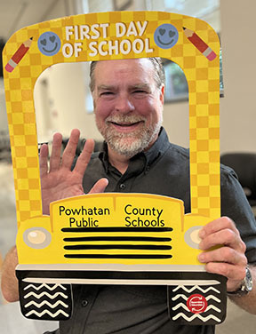 A new staff member poses with a school bus-themed First Day of School photo prop.