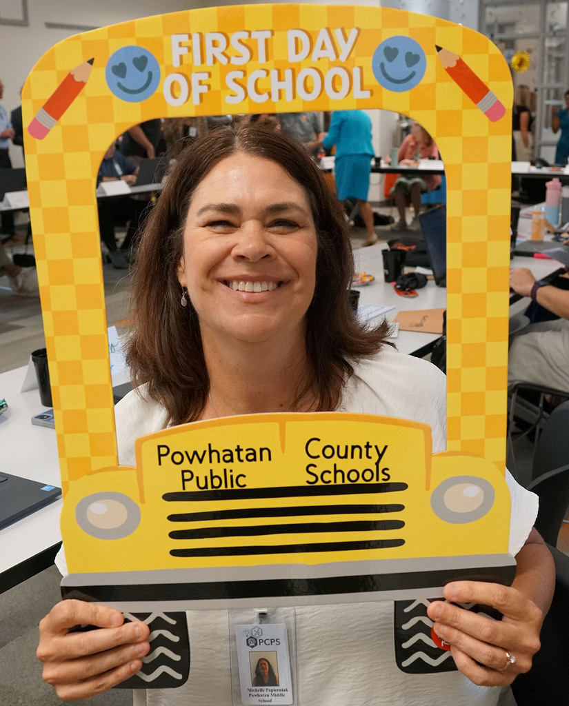 A new staff member poses with a school bus-themed First Day of School photo prop.