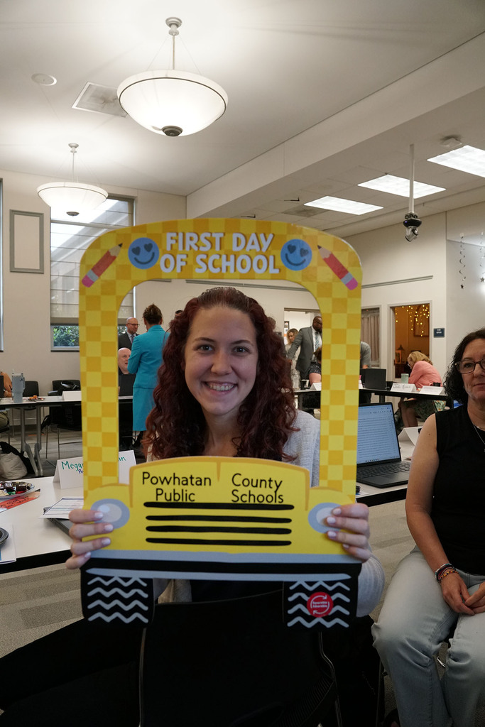 A new staff member poses with a school bus-themed First Day of School photo prop.