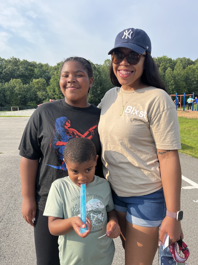 An adult takes a photo with a rising kindergartener and an older child at a kindergarten welcome event.