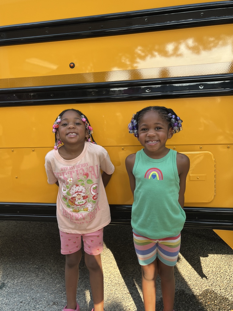 Two rising kindergarteners pose for a photo in front of a bus. 