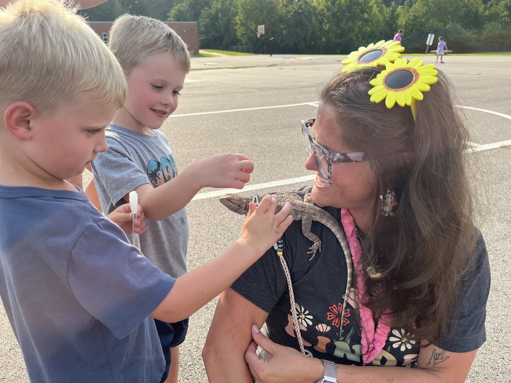 Two rising kindergarteners meet a lizard sitting on a teacher's shoulder.