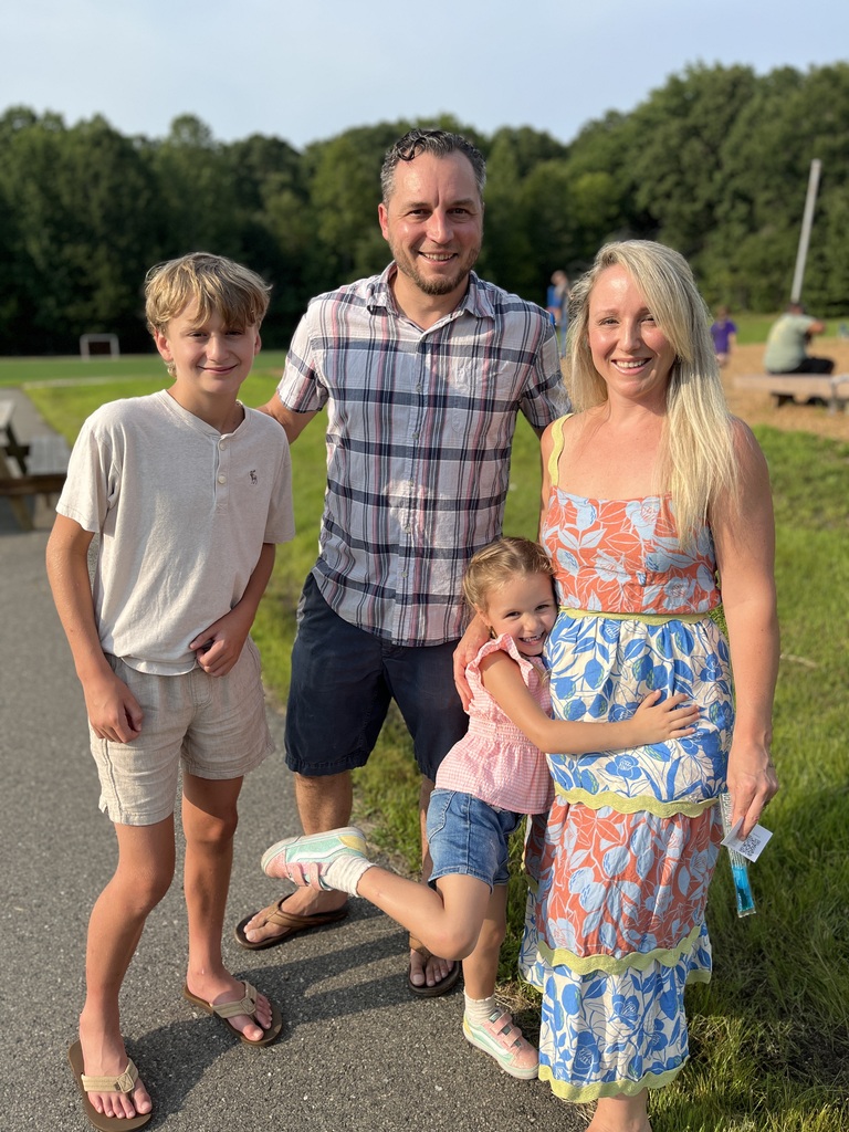 Two adults take a photo with a rising kindergartener and an older child at a kindergarten welcome event.