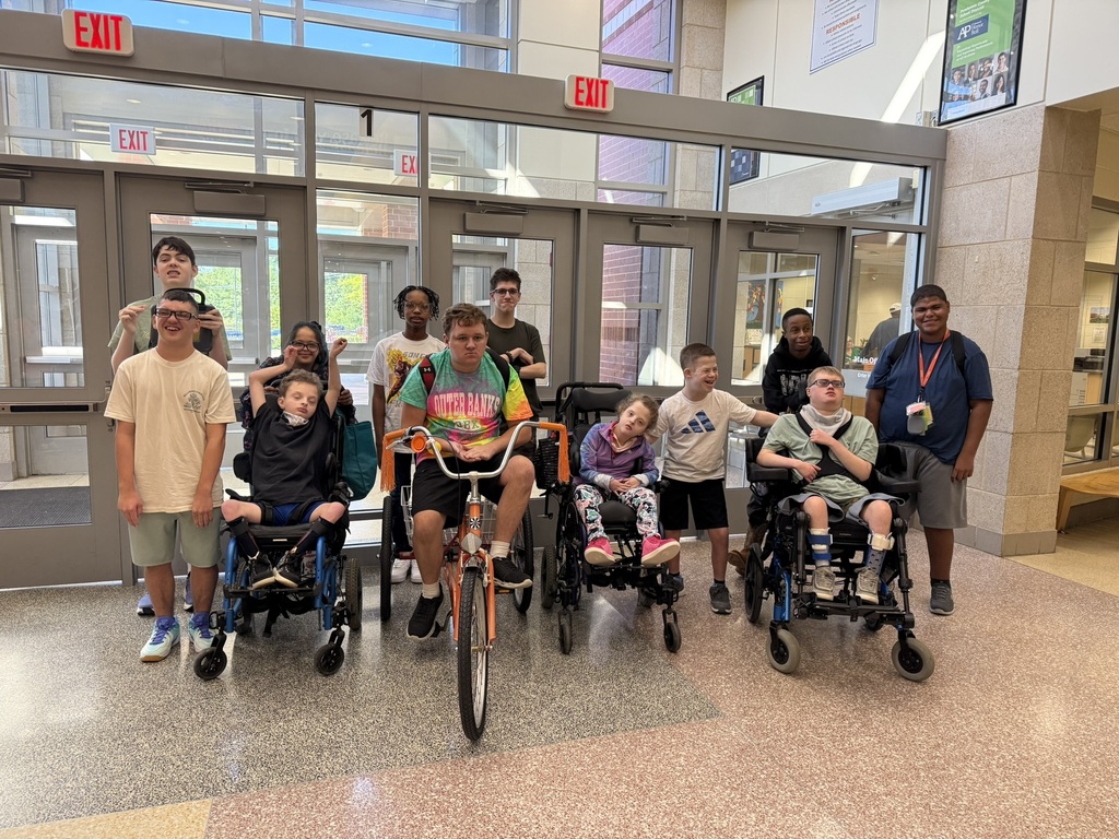 Photo of a group of students and attendants at a high school. One student is on an adult triclycle.