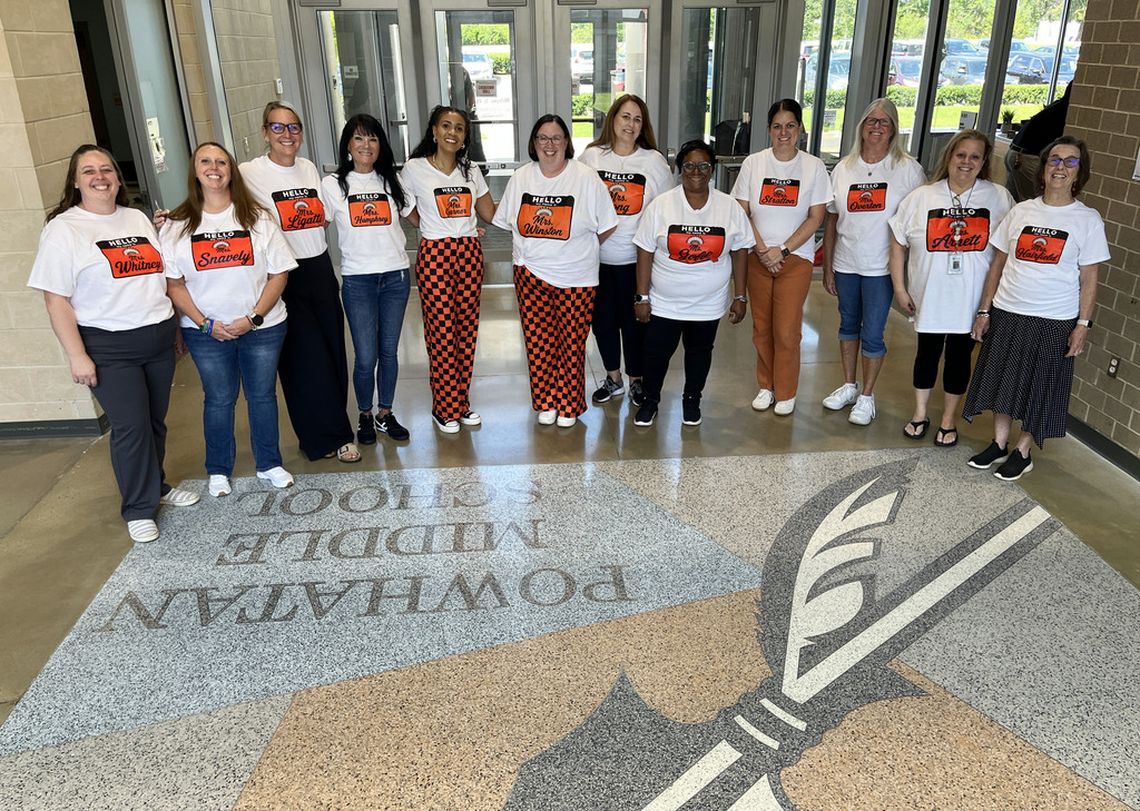 A group of teachers in matching "my name is" shirts pose for a photo in the middle school front entrance.