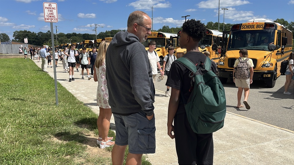A middle school staff member helps students during bus dismissal.