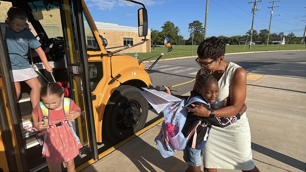 Students arrive via school bus for the first day of school. They are greeted by adults. 