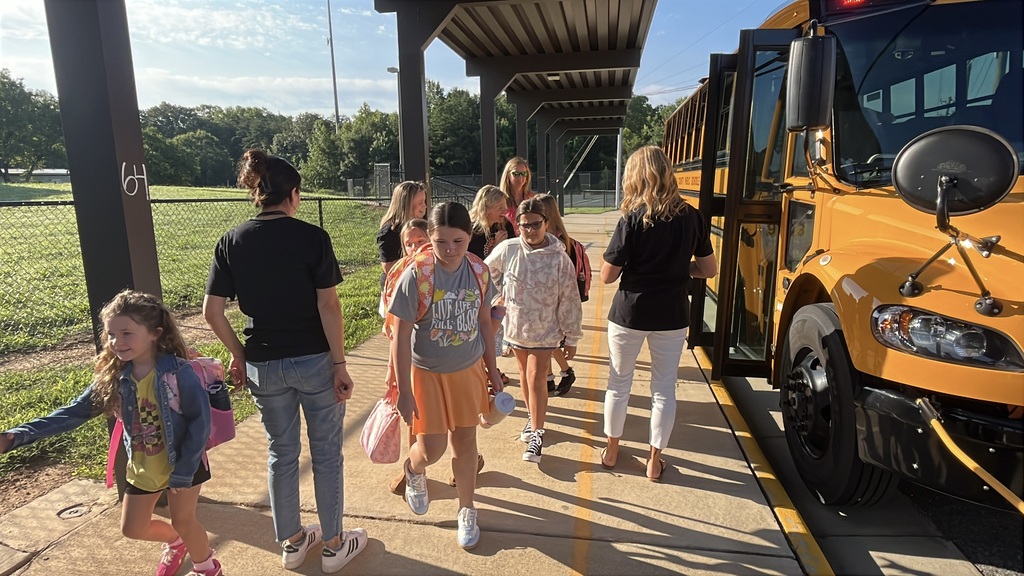 Students arrive via school bus for the first day of school. They are greeted by adults. 
