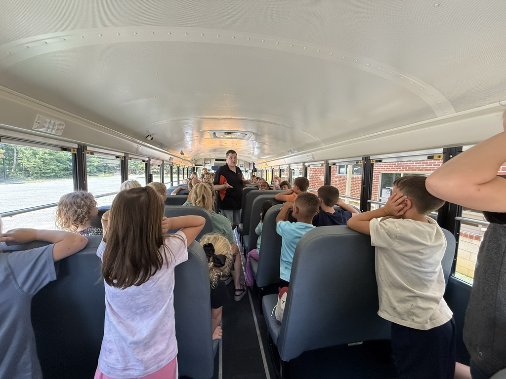 A bus driver on a school bus talks to a group of first graders about bus safety.