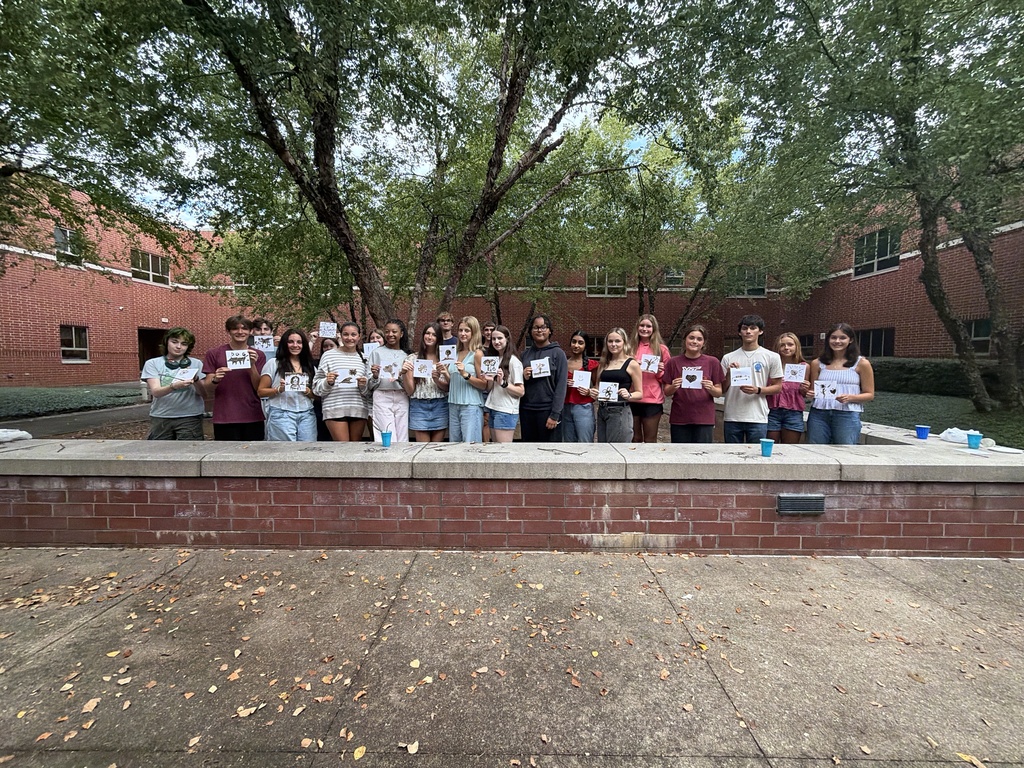 A group of art students in a courtyard hold paintings they made inspired by prehistoric art.