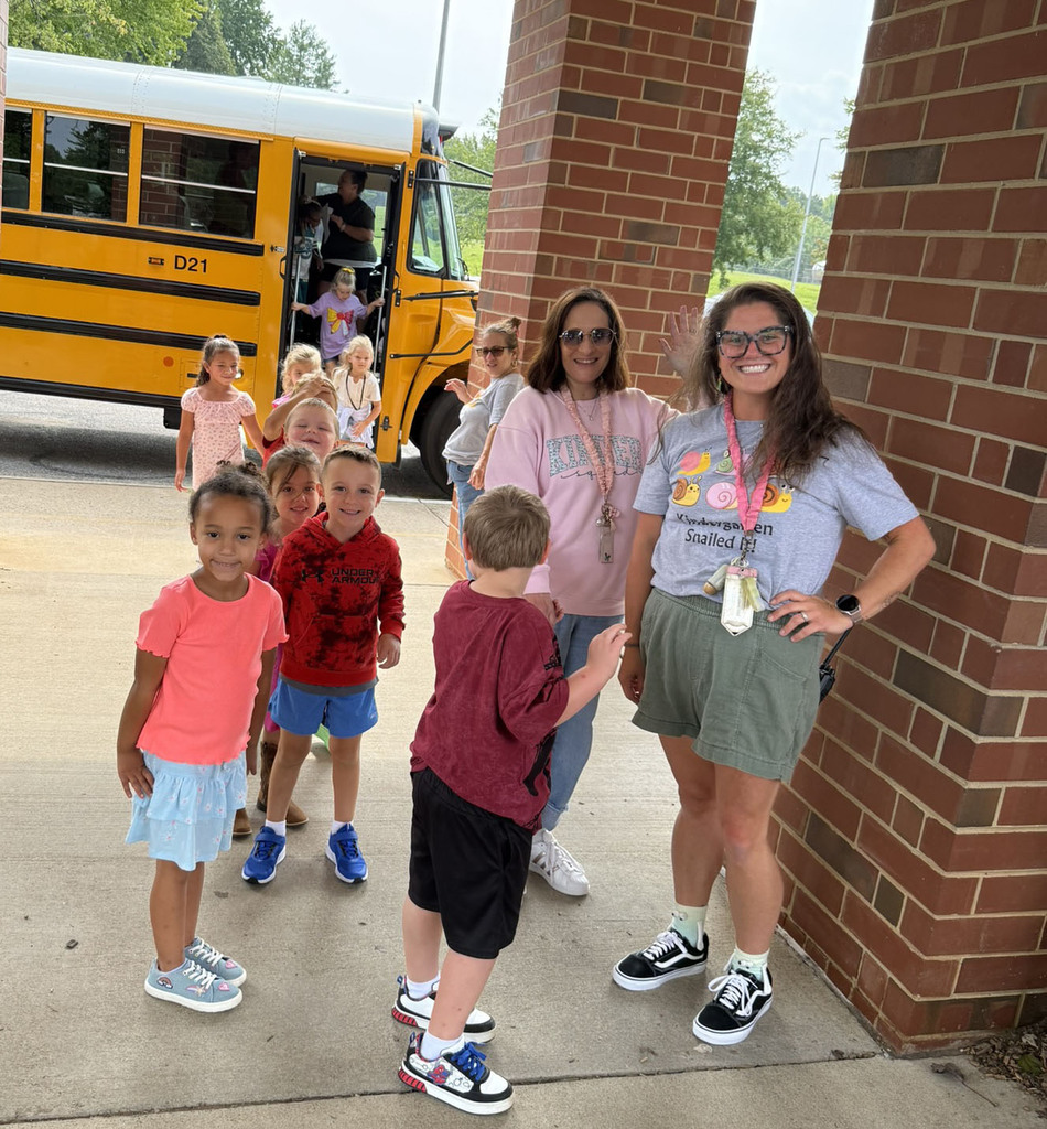 A line of kindergarten students and teachers poses for a photo in front of a school bus.