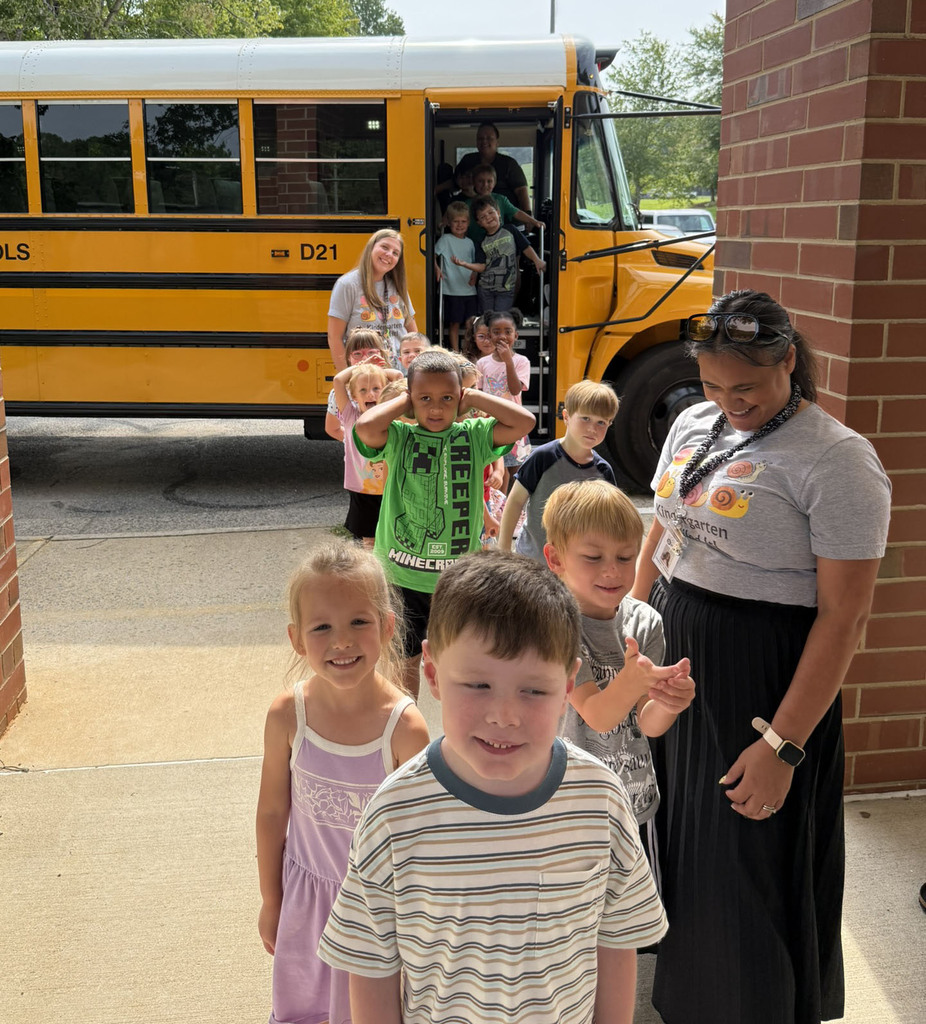 A line of kindergarten students and teachers poses for a photo in front of a school bus.