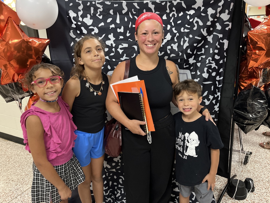 An adult and three children pose for a photo in front of a photo display at an elementary open house. 