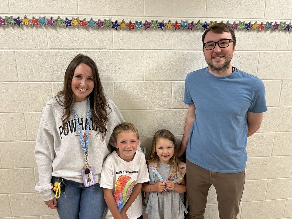 Two adults and two children pose for a photo in front of a photo display at an elementary open house. 