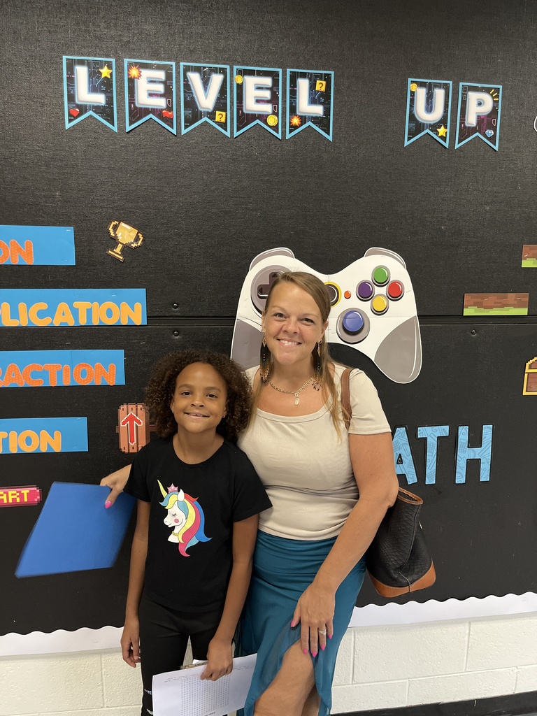 An adult and a child pose for a photo in front of a photo display at an elementary open house. 