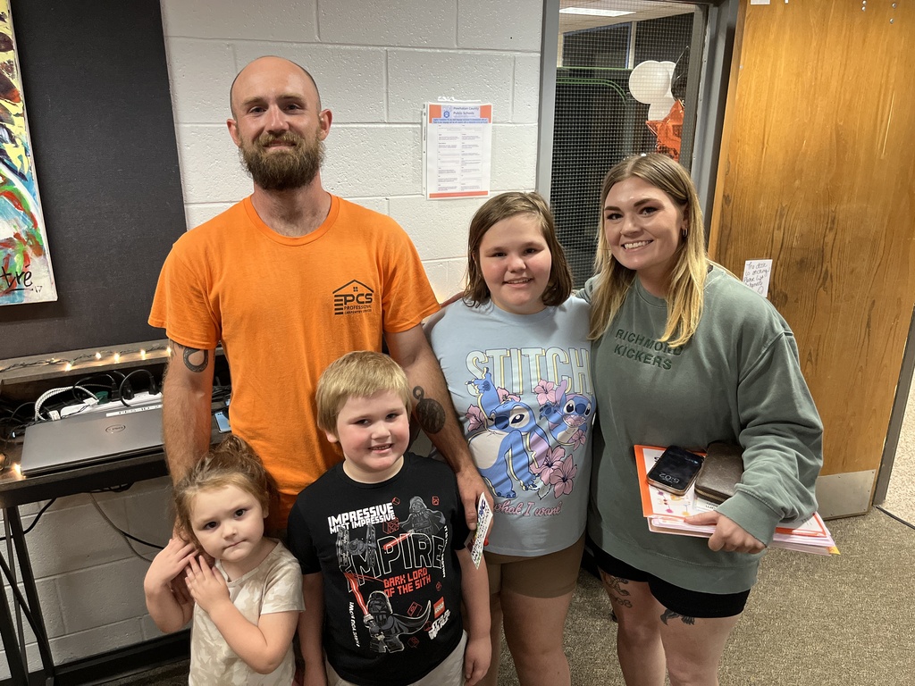 Two adults and three children pose for a photo in front of a photo display at an elementary open house. 