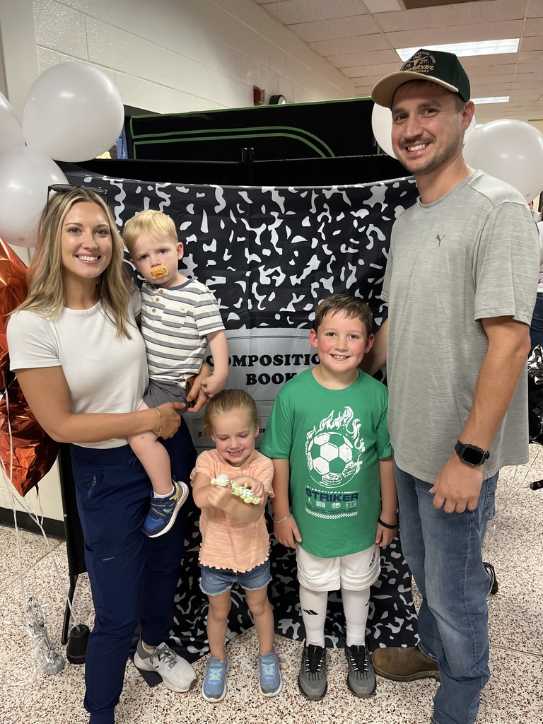 Two adults and three children pose for a photo in front of a photo display at an elementary open house. 