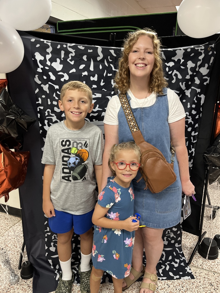 An adult and two children  pose for a photo in front of a photo display at an elementary open house. 