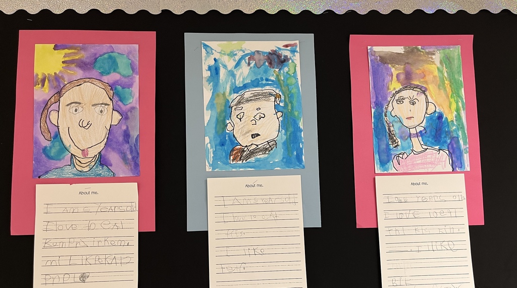 Photo of student work posted in a hallway. Features self portraits they drew and a writing assignment to tell about themselves.