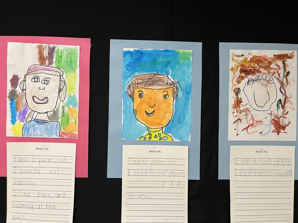 Photo of student work posted in a hallway. Features self portraits they drew and a writing assignment to tell about themselves.