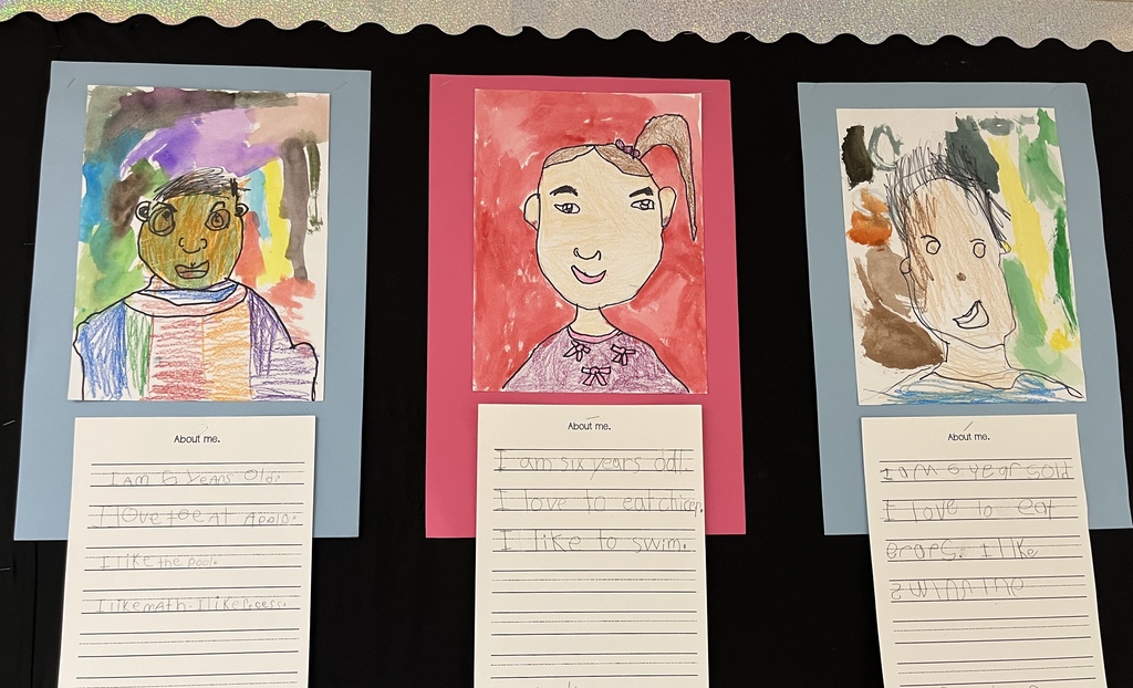 Photo of student work posted in a hallway. Features self portraits they drew and a writing assignment to tell about themselves.