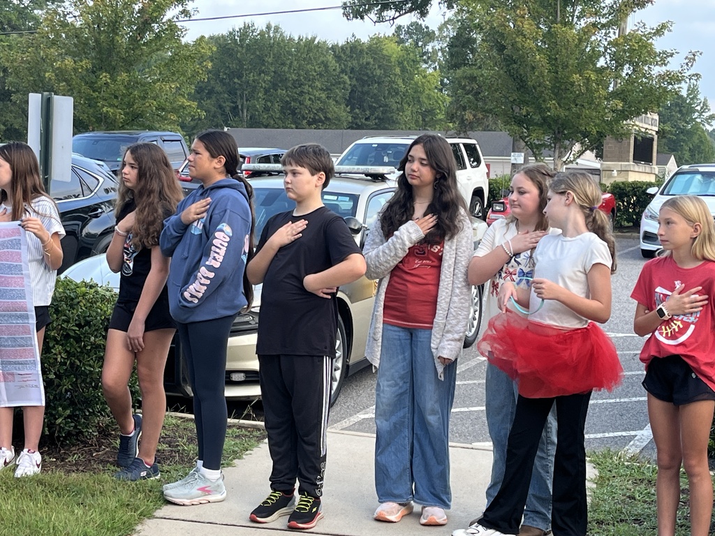 Students  recite the pledge of allegiance during a 9/11 ceremony held in front of a middle school.