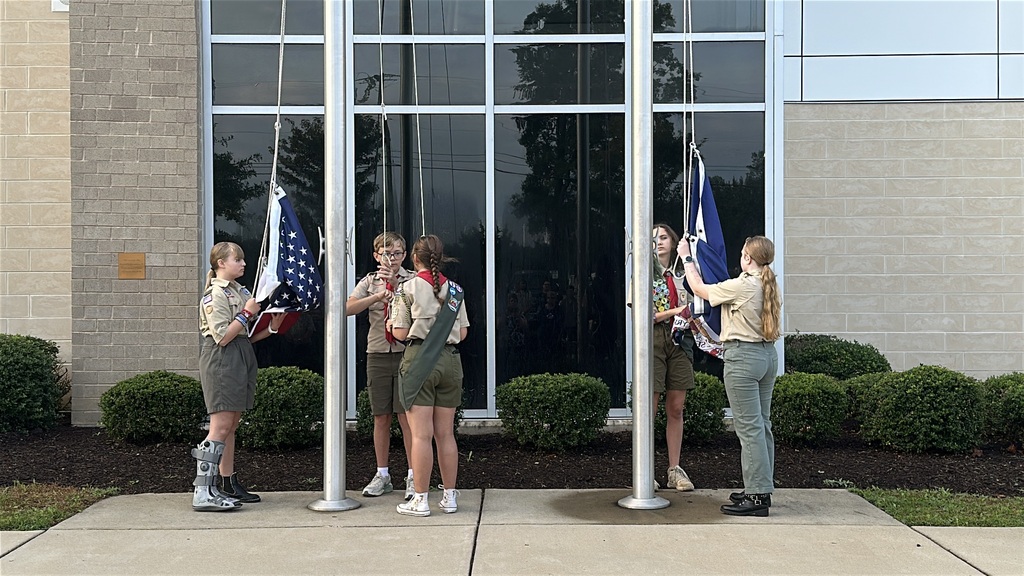 Scouting America members raise the flag during a 9/11 ceremony held in front of a middle school. 