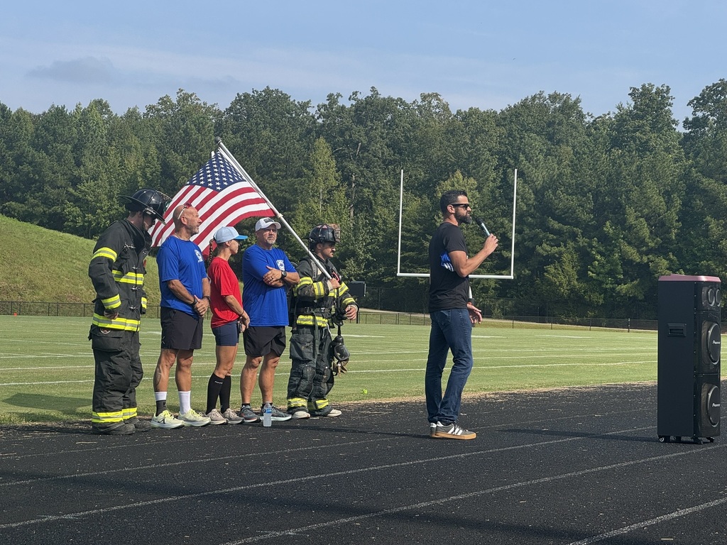 The principal kicks off a 9/11 ceremony at his high school. Behind him are organizers and participants of a remembrance run. 