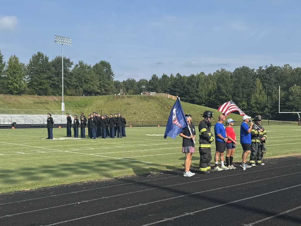 Organizers and participants of a 9/11  remembrance run hold a kickoff ceremony. A JROTC battalion stands at attention behind them.