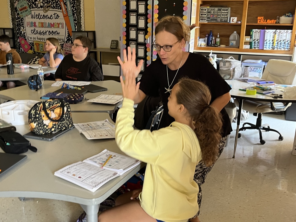 Fifth graders listen to a lesson from their teacher on the law of conservation of matter. A staff member and child give high fives.
