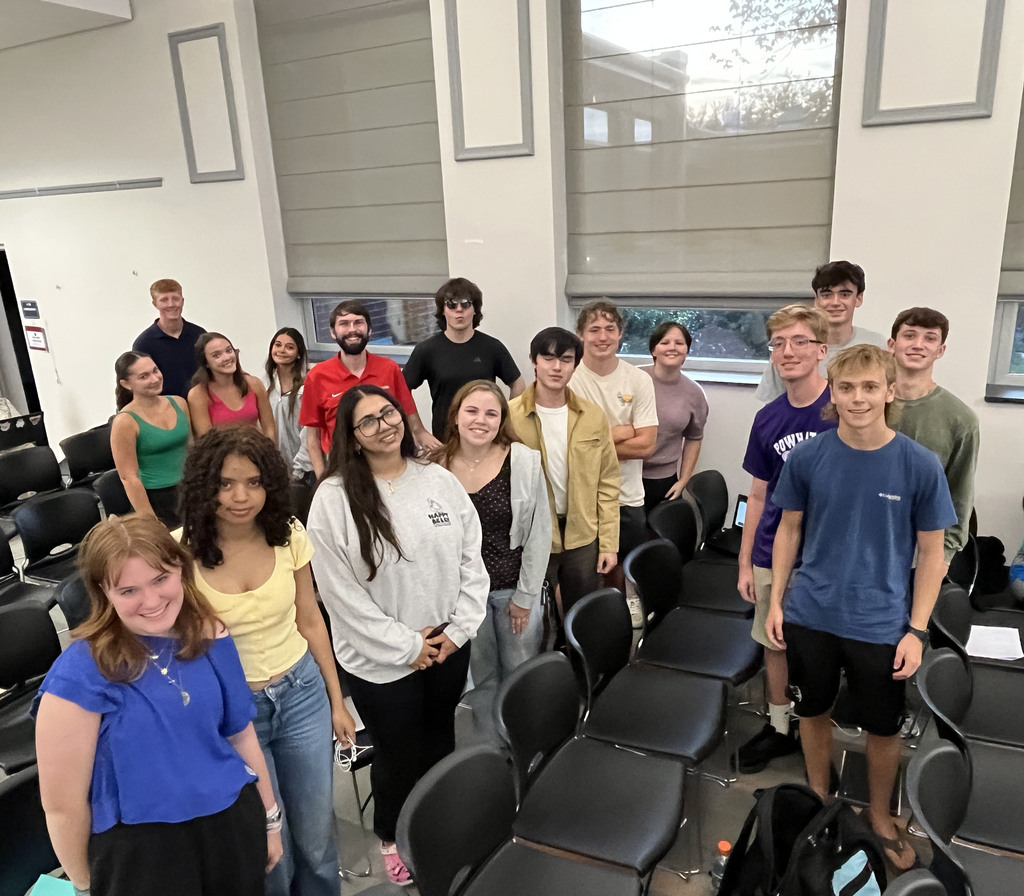 A group of students and a teacher in a board room pose for a group photo.