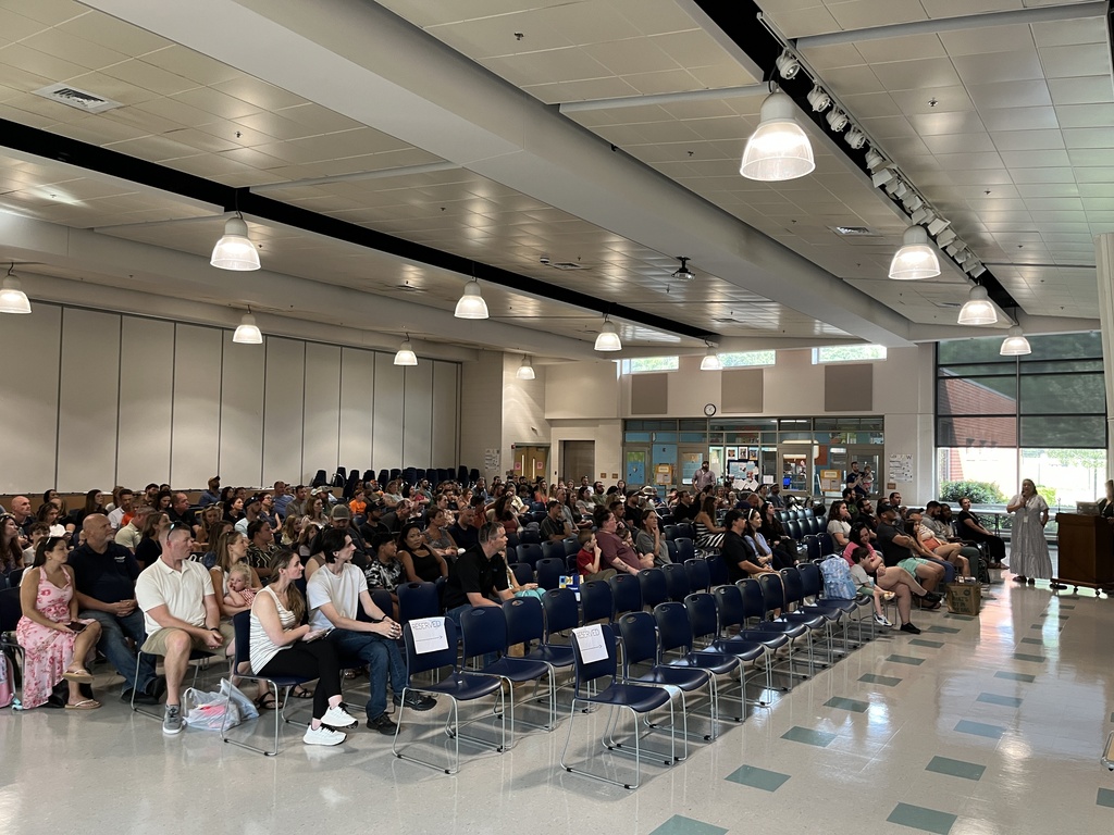 A room full of families listen to their child's elementary school principal speak at an open house event. 
