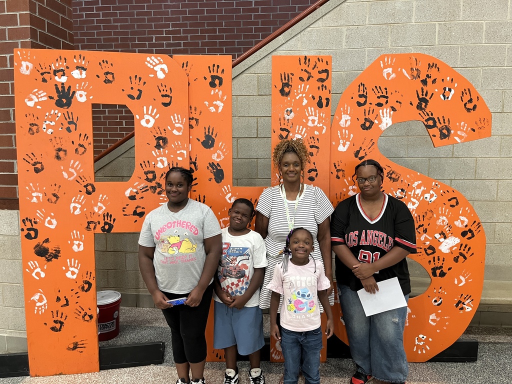 An adult and four children pose for a photo in front of a large orange PHS backdrop at a high school open house event.