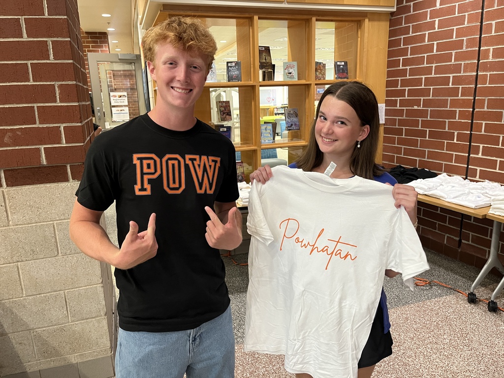 Two teenagers pose for a photo while promoting tshirt sales at a high school open house event.