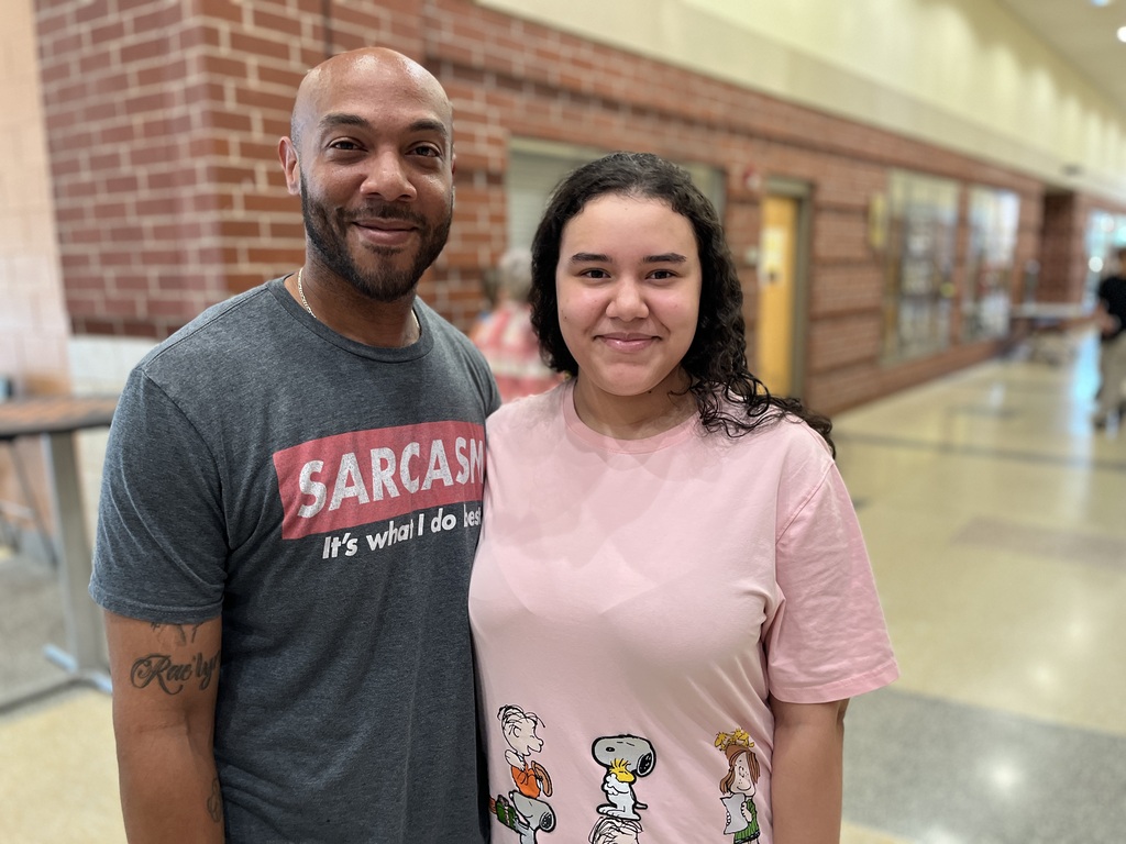 An adult and a teen pose for a photo at a high school open house event.