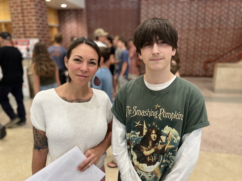 An adult and a teen pose for a photo at a high school open house event.