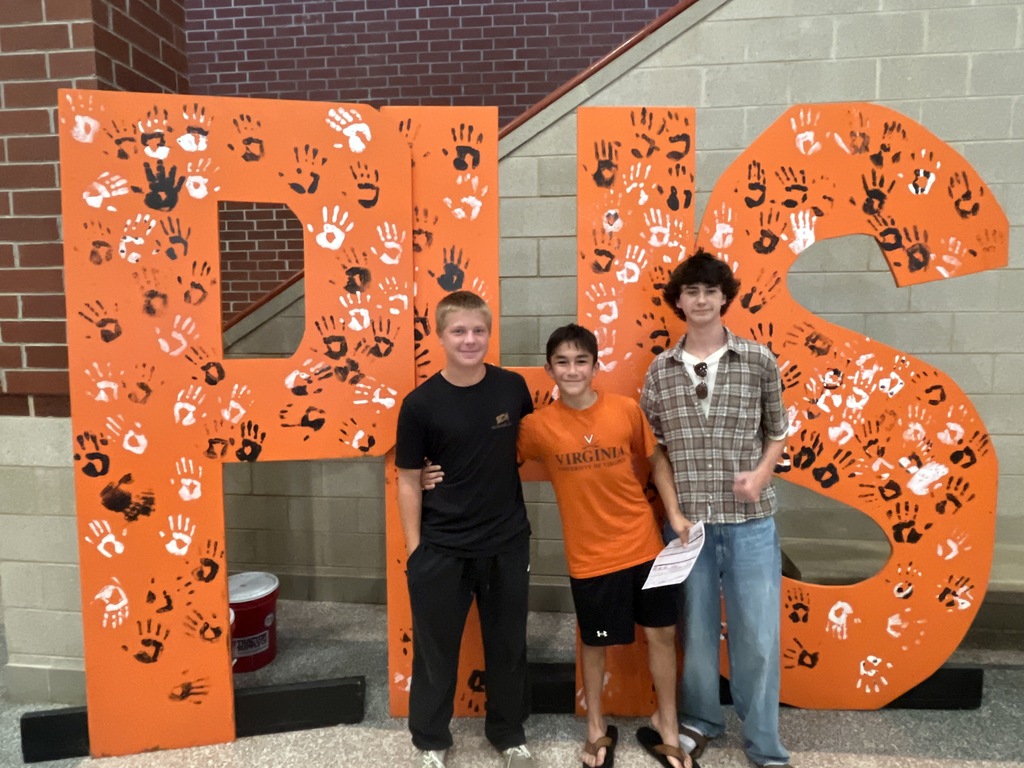 Three teenagers pose for a photo in front of a large orange PHS backdrop at a high school open house event.