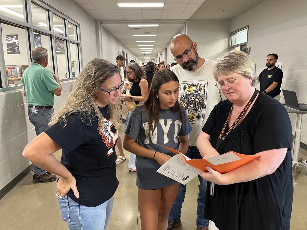 A middle school staff member gives information to a family at a middle school open house. 
