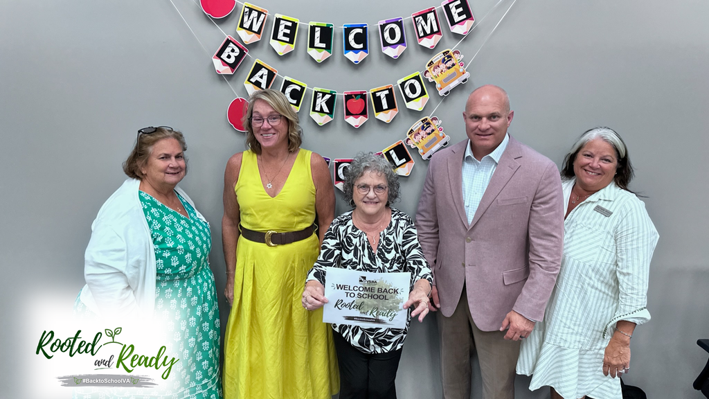 Five school board members  pose for a photo in front of a Welcome Back to School sign. Text embedded in photo: Rooted and Ready. 