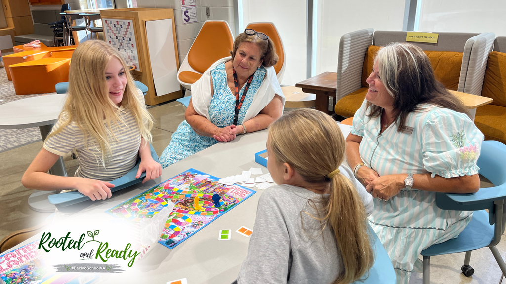 Two school board members watch students play a game. Text embedded in photo: Rooted and Ready. 