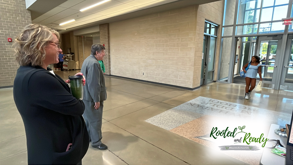 A school board member and superintendent welcome a student to school. Text embedded in photo: Rooted and Ready. 