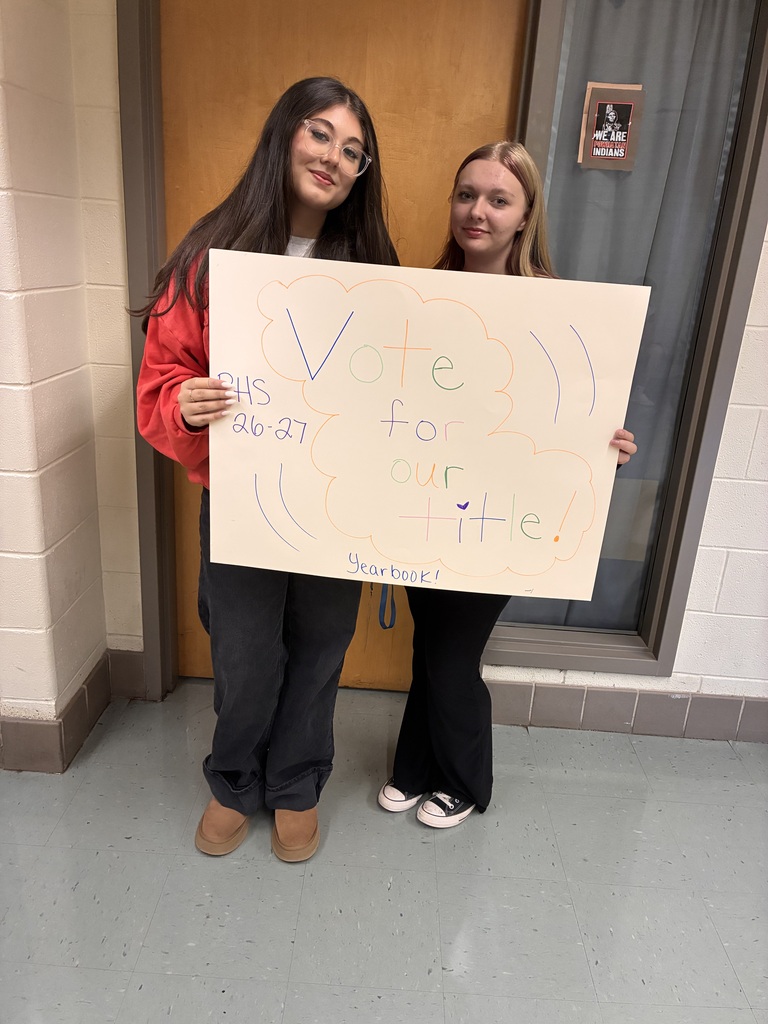 Two students hold a sign that reads Vote for our title! Yearbook. PHS 26-27.