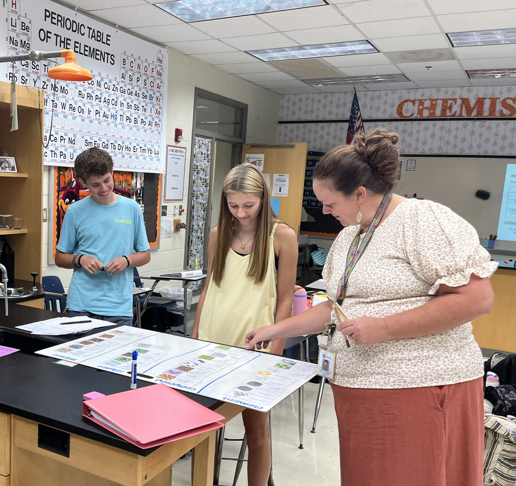 Chemistry students participate in a station exercise where they practice classifying the different types of matter. A teacher checks their work.