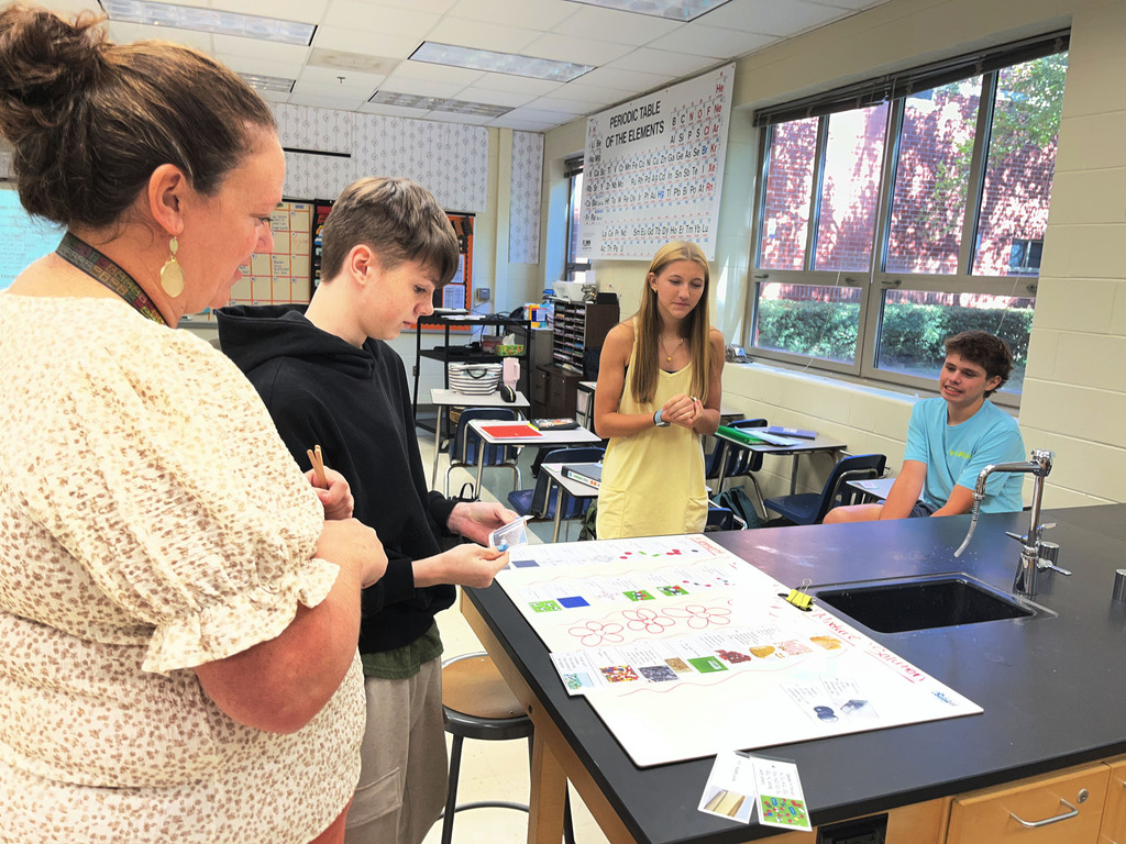 Chemistry students participate in a station exercise where they practice classifying the different types of matter. A teacher checks their work.