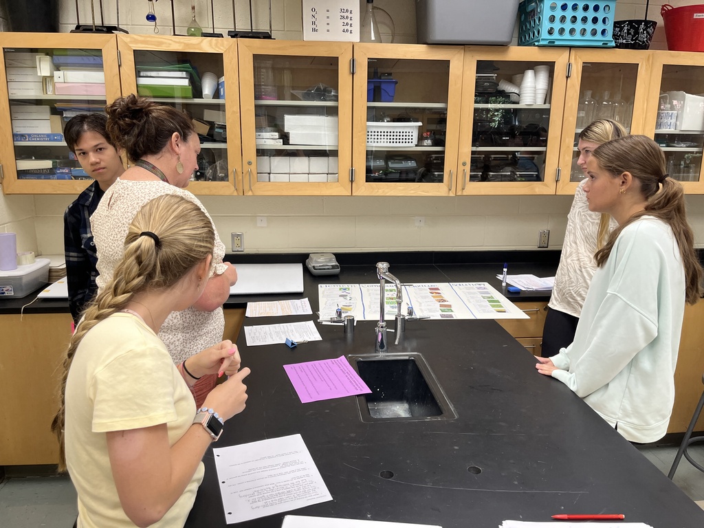 Chemistry students participate in a station exercise where they practice classifying the different types of matter. A teacher checks their work.