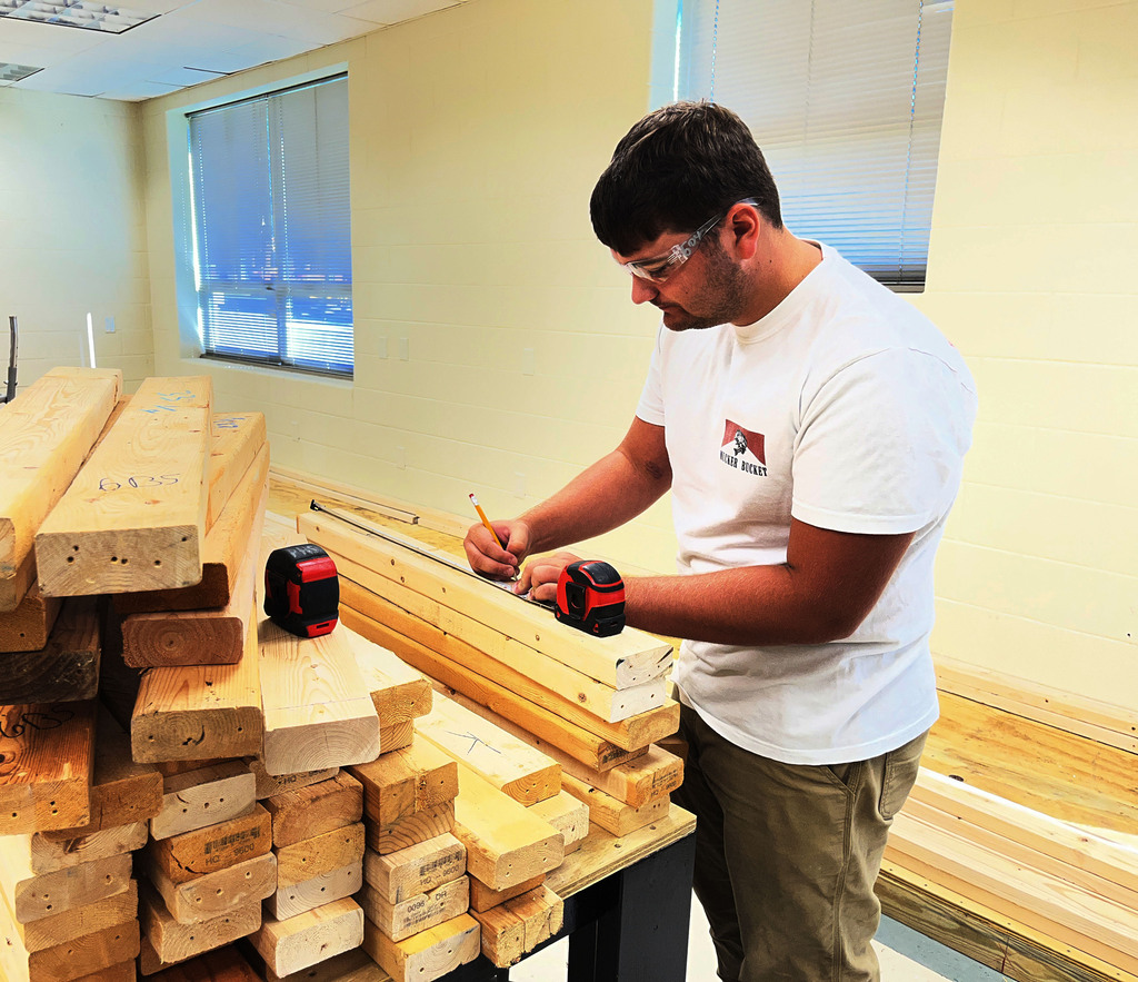 A building trades student measures  wood that will be used to build electricity booths. 
