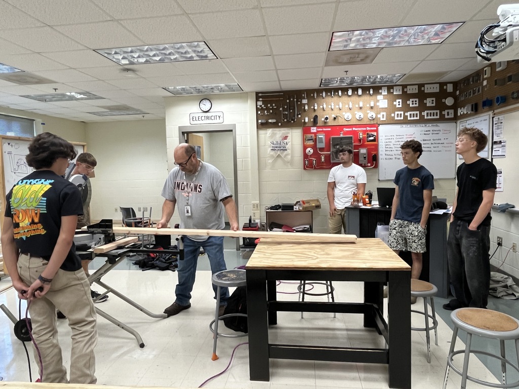 A teacher demonstrates how to use a saw to building trades students building electricity booths. 