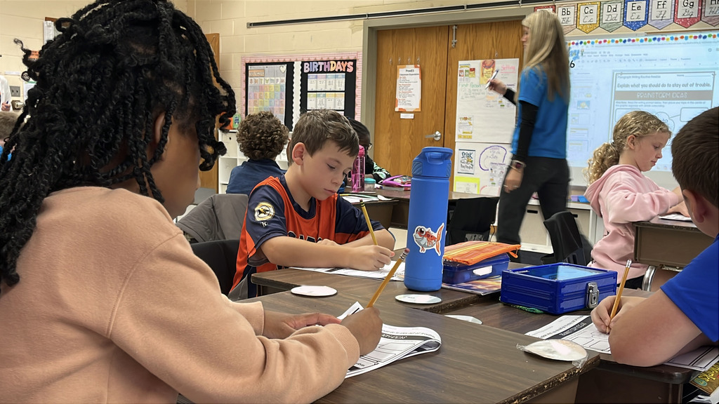 Students brainstorm ideas for a writing prompt about how to stay out of trouble . A teacher observes.
